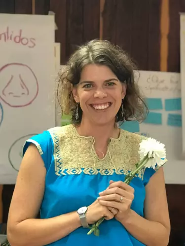 Joanna stands in front of some hand-drawn posters holding a white flower
